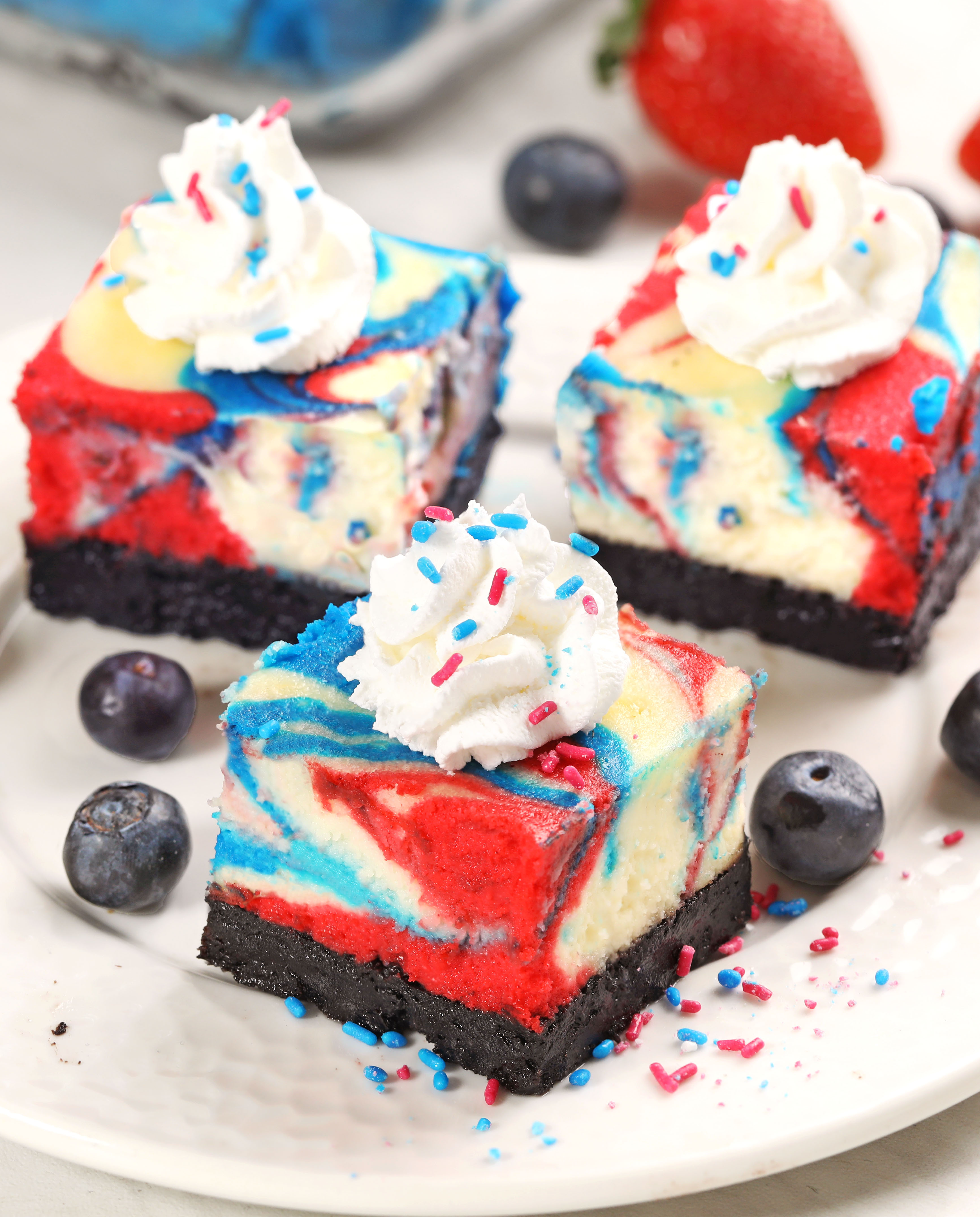 Celebrate 4th of July with these red, white & blue cheesecake swirled bars! Creamy vanilla cheesecake with an Oreo crust, swirled with bold patriotic colors and baked to perfection in a water bath.